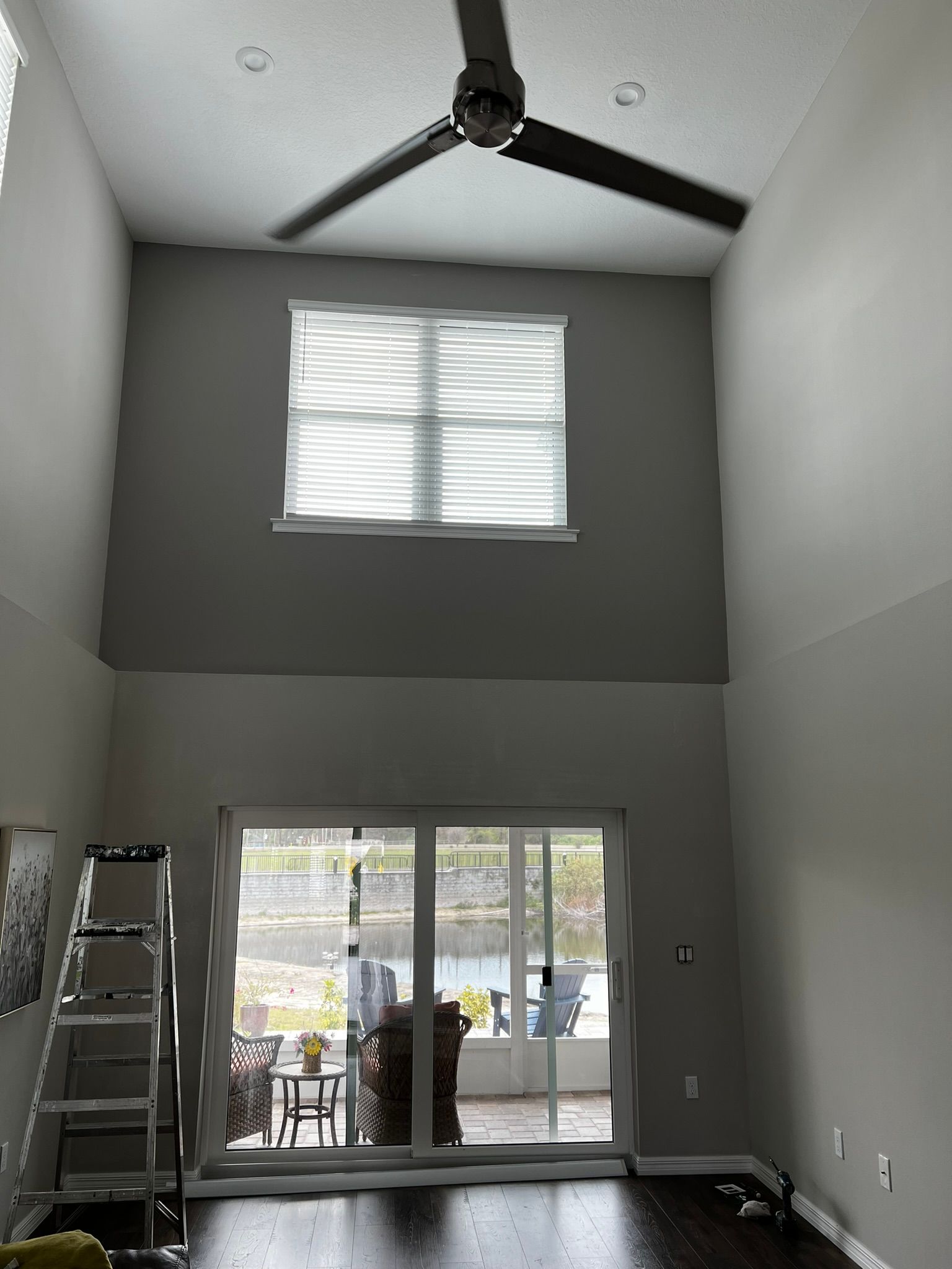 A living room with tall ceilings, a window, and a sliding glass door overlooking a patio.