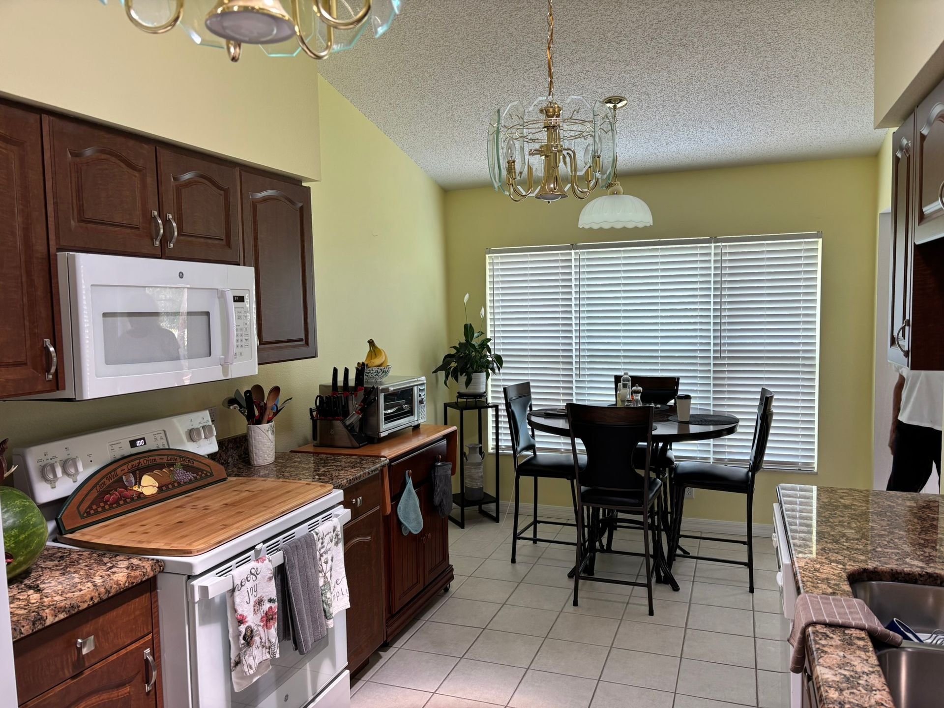 Kitchen with dark cabinets, white appliances, round table near window, and patterned countertops.