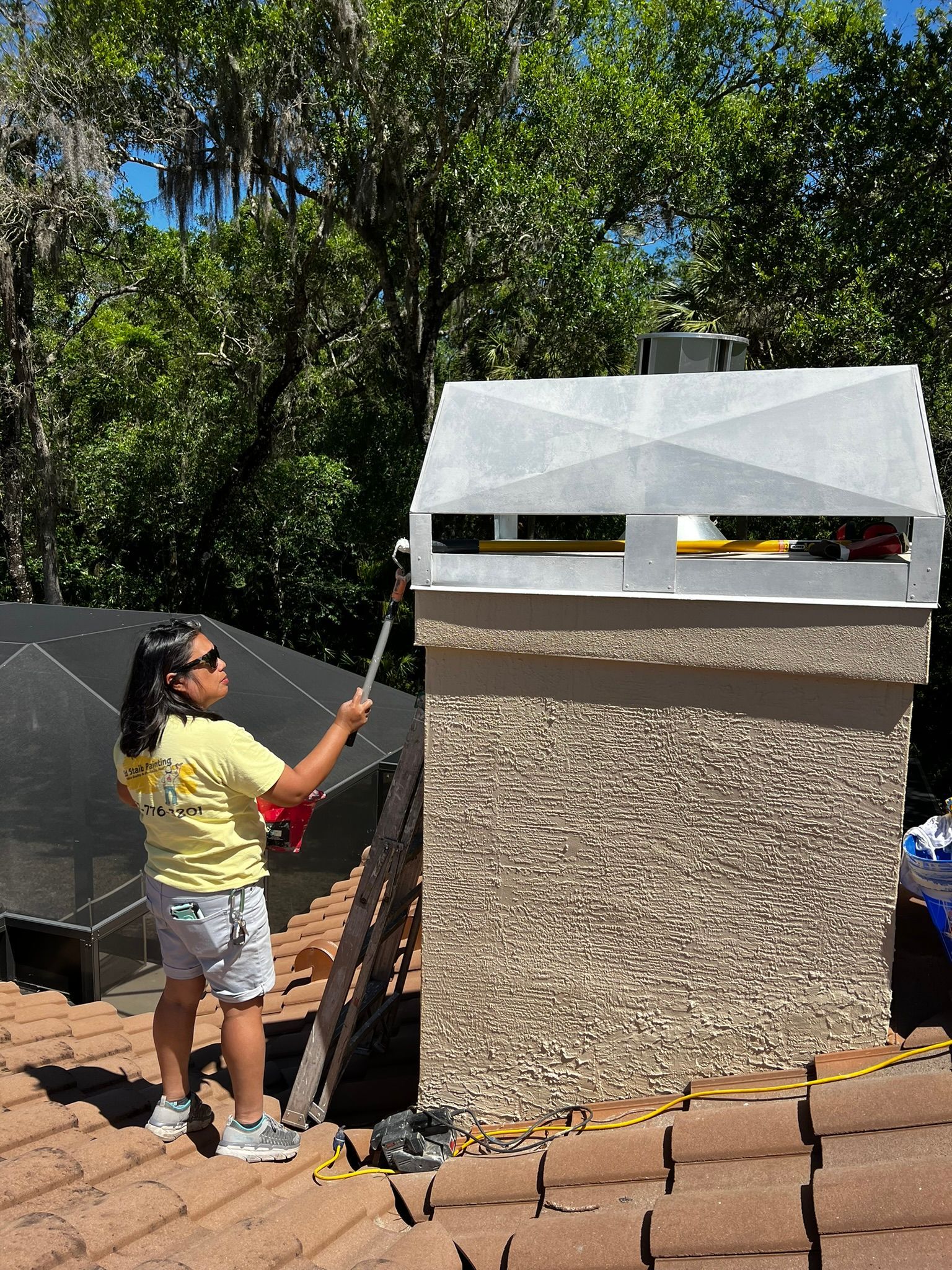 Woman on a roof cleaning a chimney with a brush. Bright sunny day.