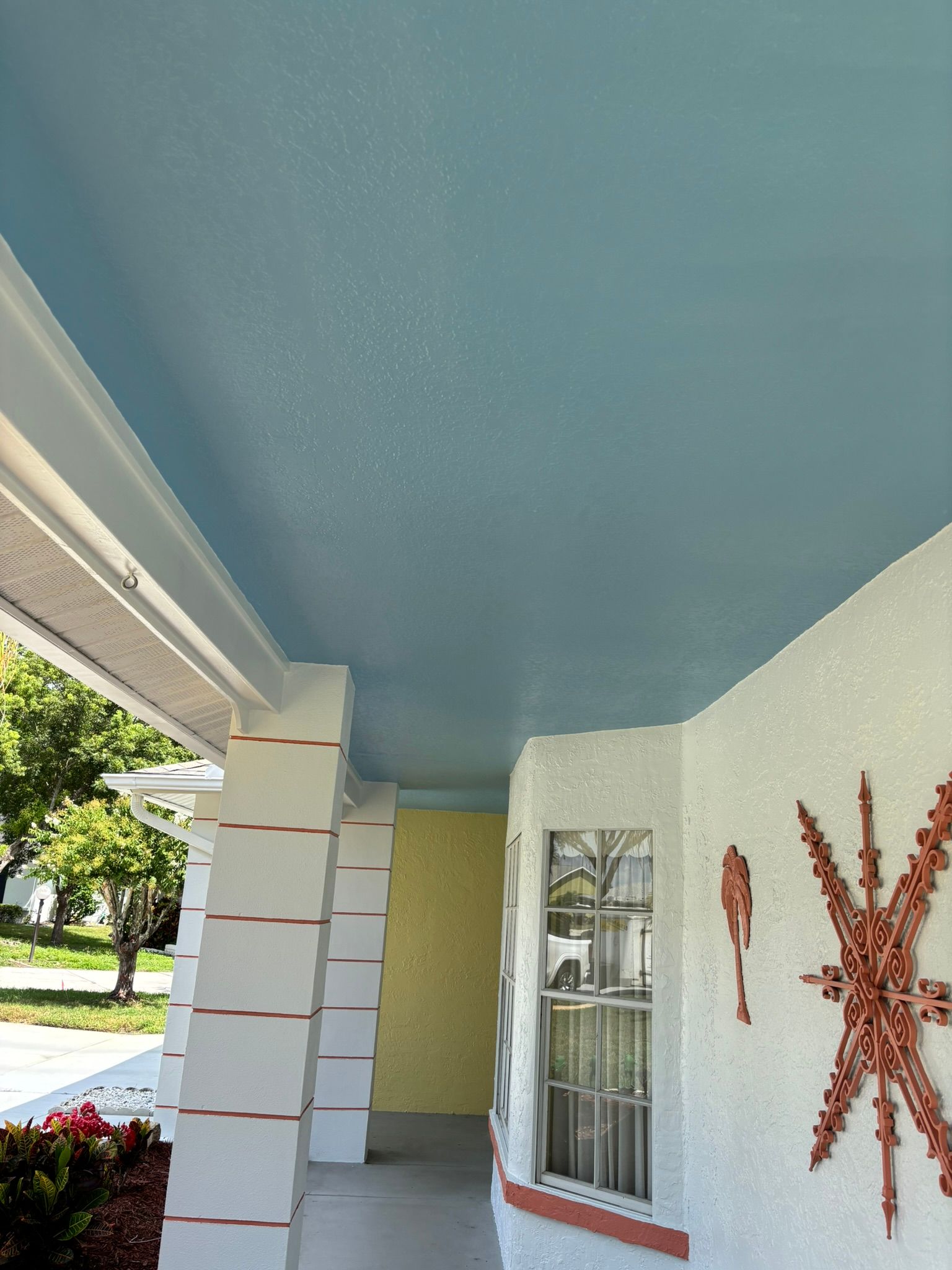 Blue porch ceiling and white pillars on a stucco house with decorative art.