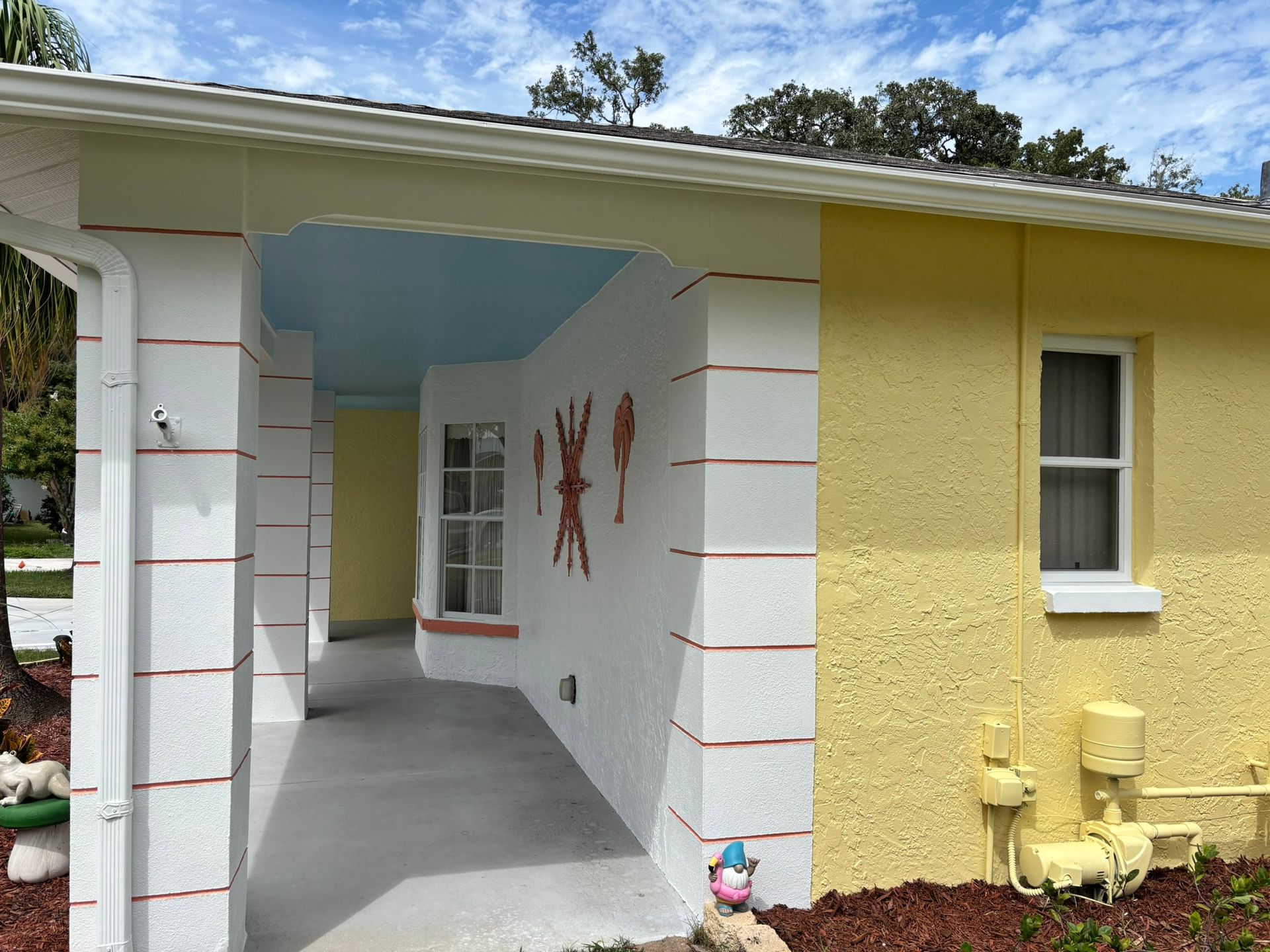 Yellow and white house exterior with blue ceiling, columns, and small window.