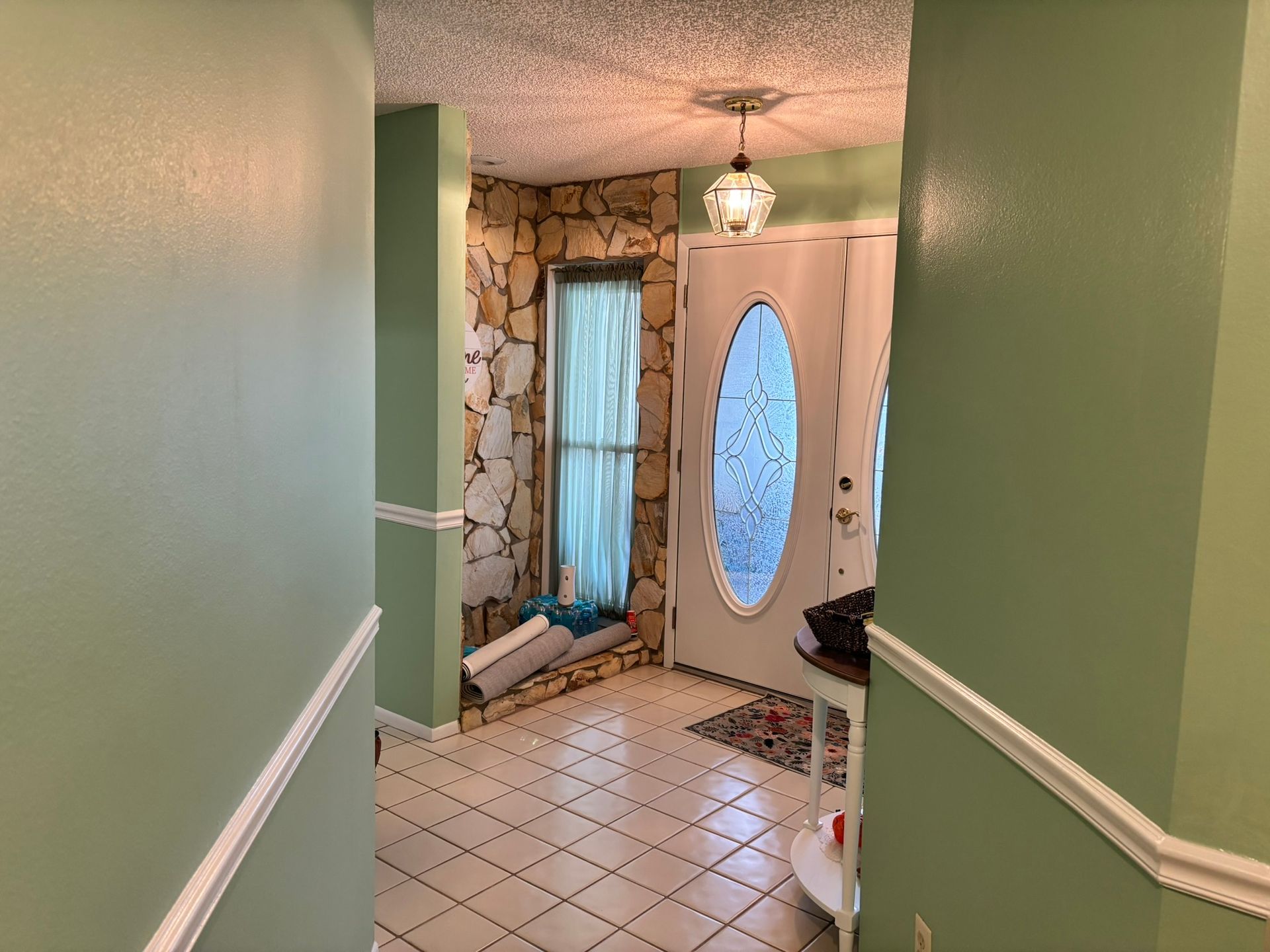 Entryway with light green walls, white trim, stone accent wall, oval-shaped front door, and textured ceiling.