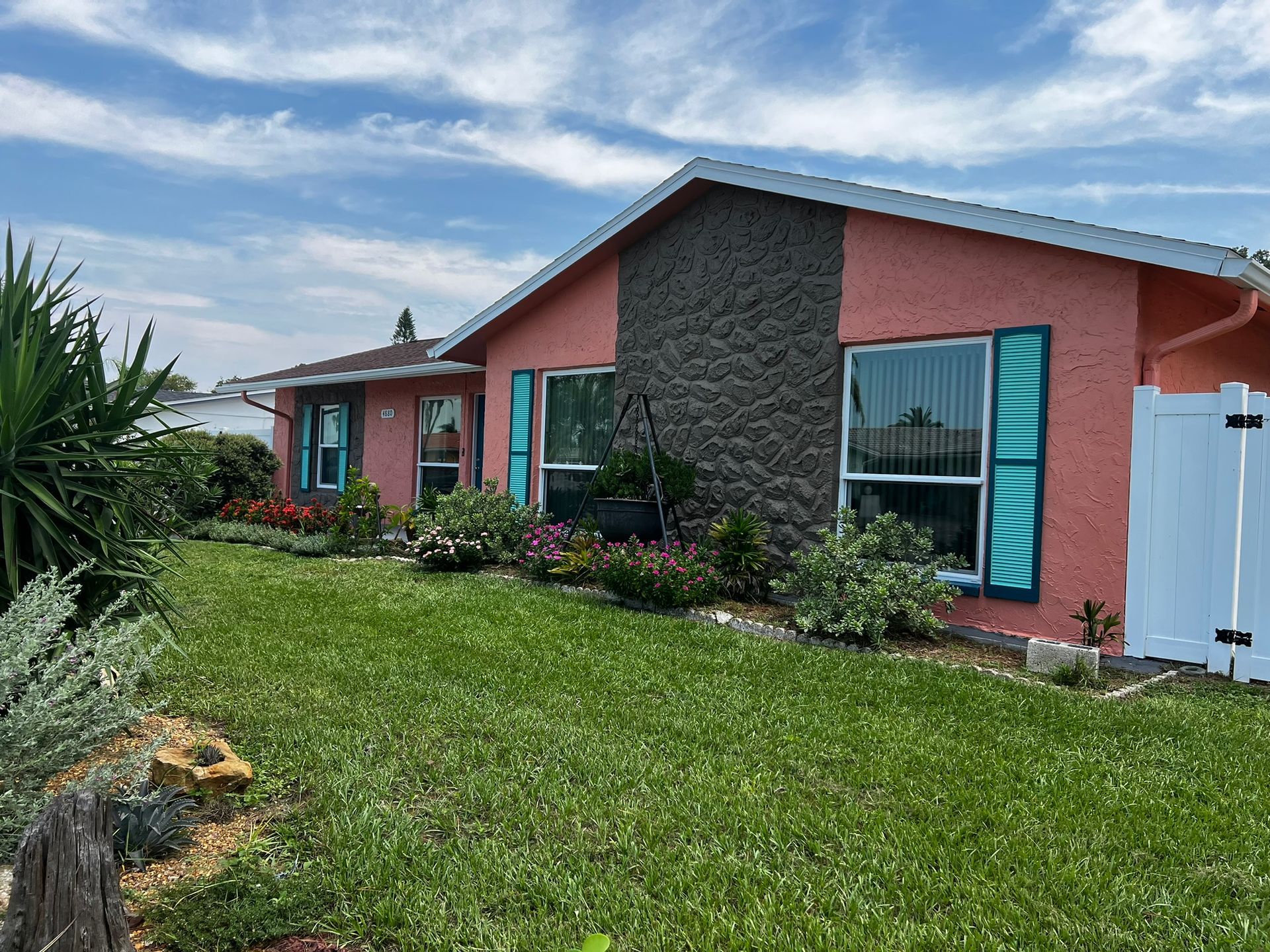 Coral-colored house with teal shutters, stone facade, and green lawn under a blue sky.
