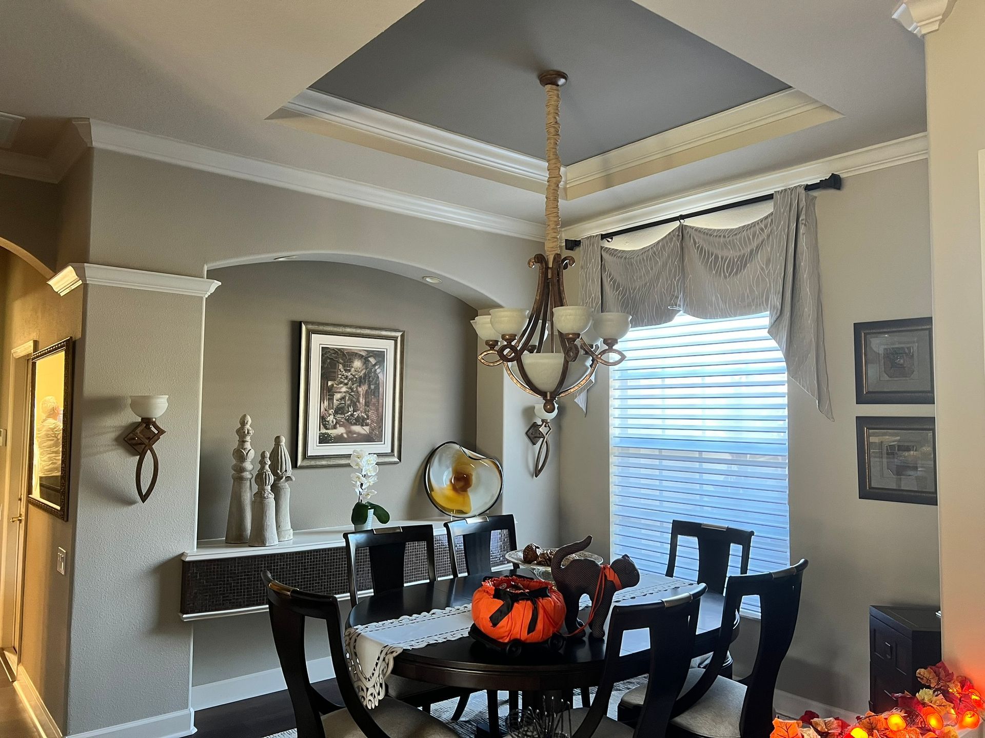 Dining room with table, chairs, chandelier, and pumpkin decor. Beige walls, white trim, and gray ceiling.