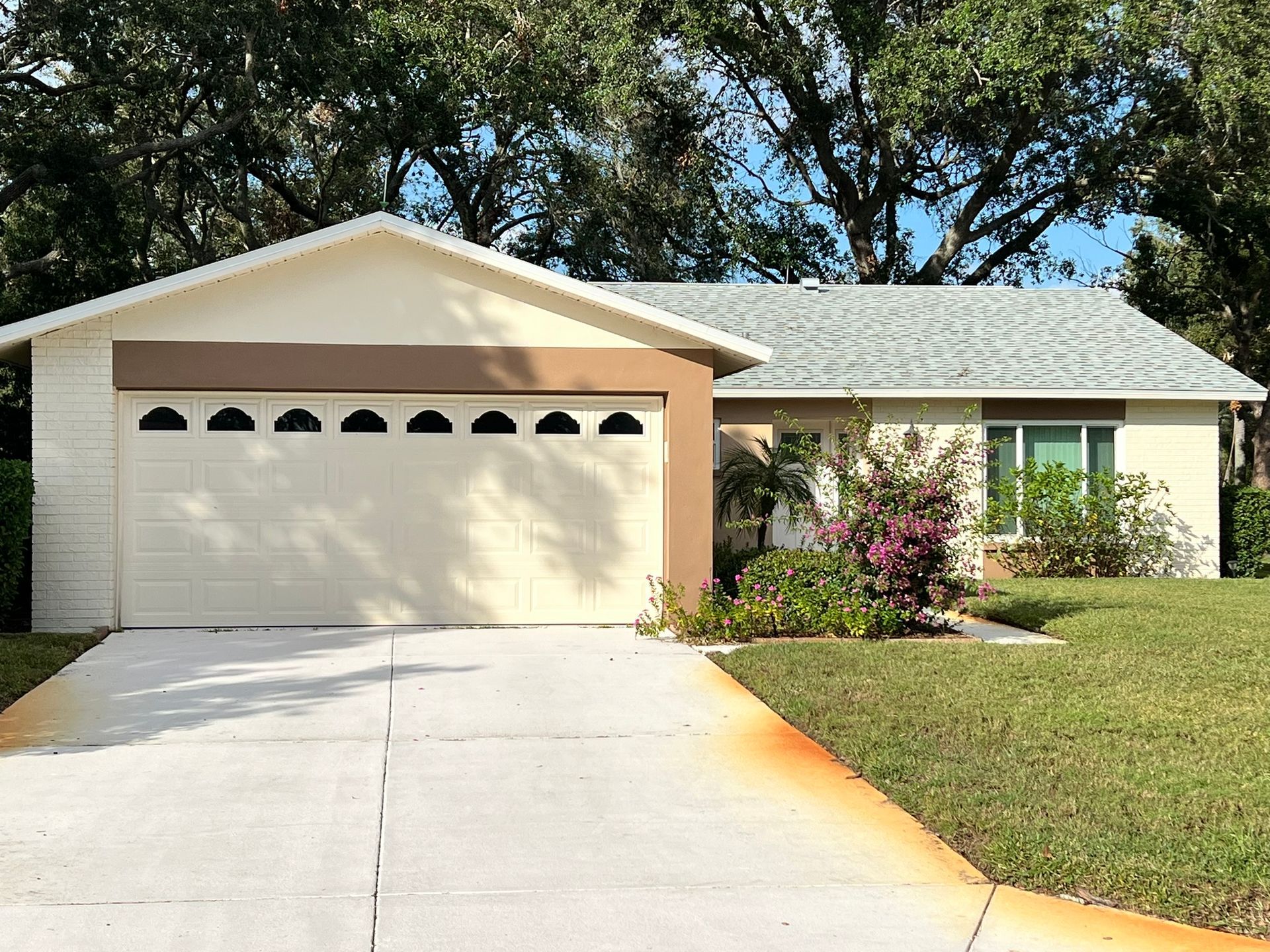 Tan ranch-style house with a two-car garage, green lawn, and blue sky in the background.