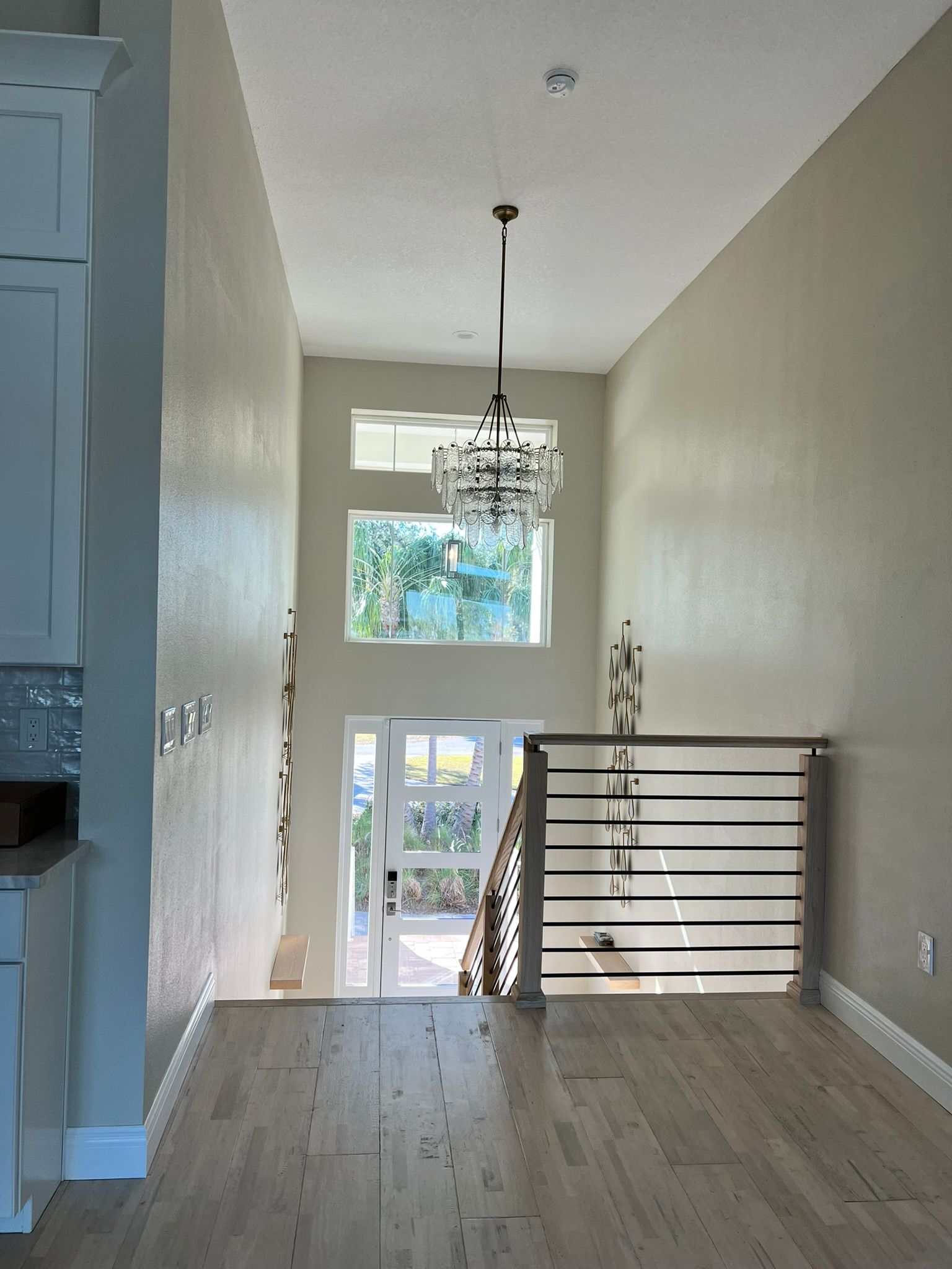 Two-story entry hall with a chandelier, staircase, and windows. Light-colored walls and wood floors.