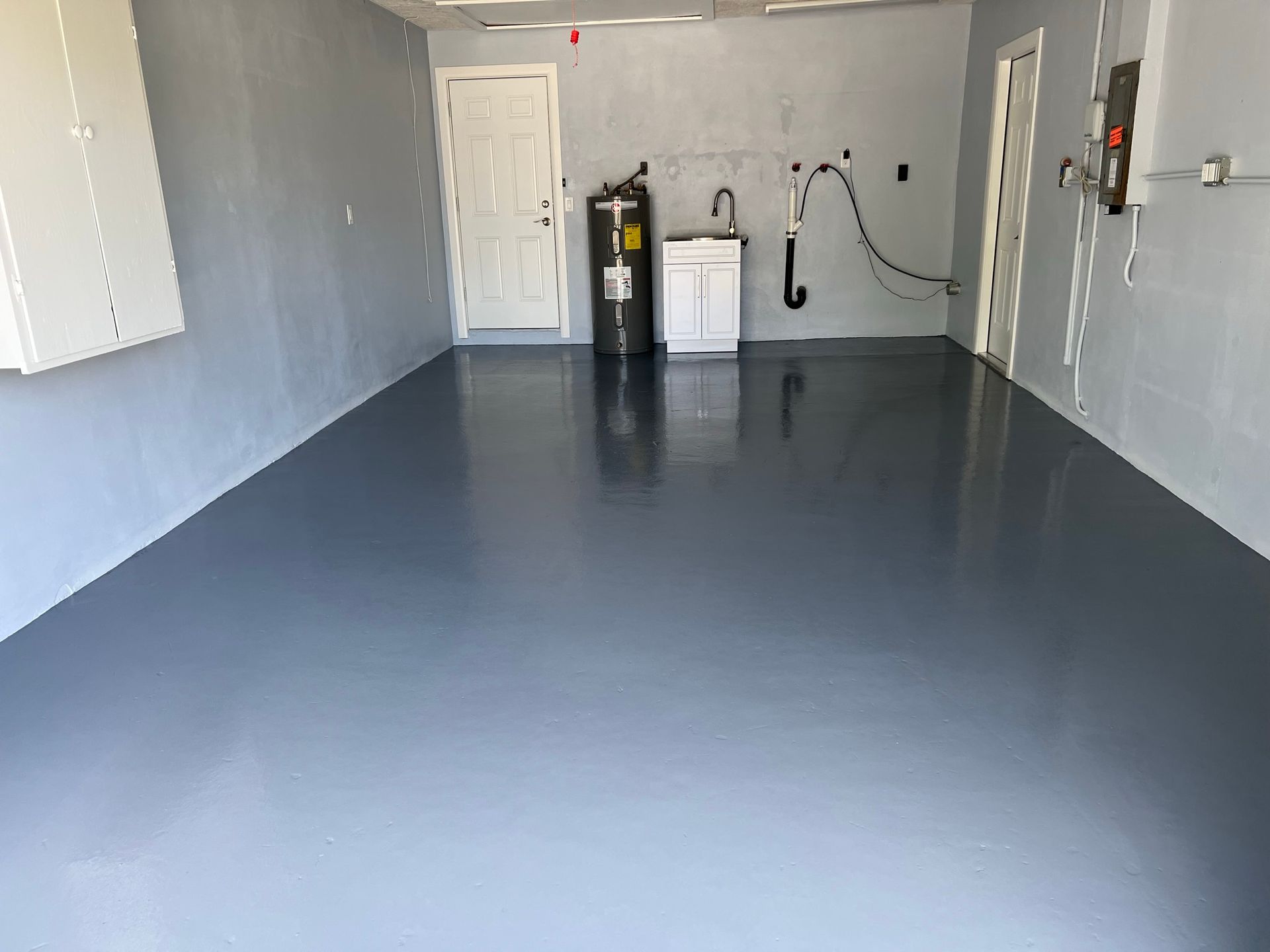 Garage with a newly painted gray floor, white door, water heater, and sink.