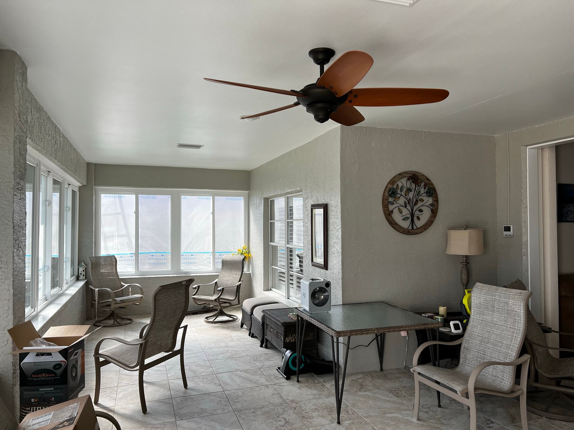 Sunroom with chairs, table, and ceiling fan; windows and a decorative wall hanging.