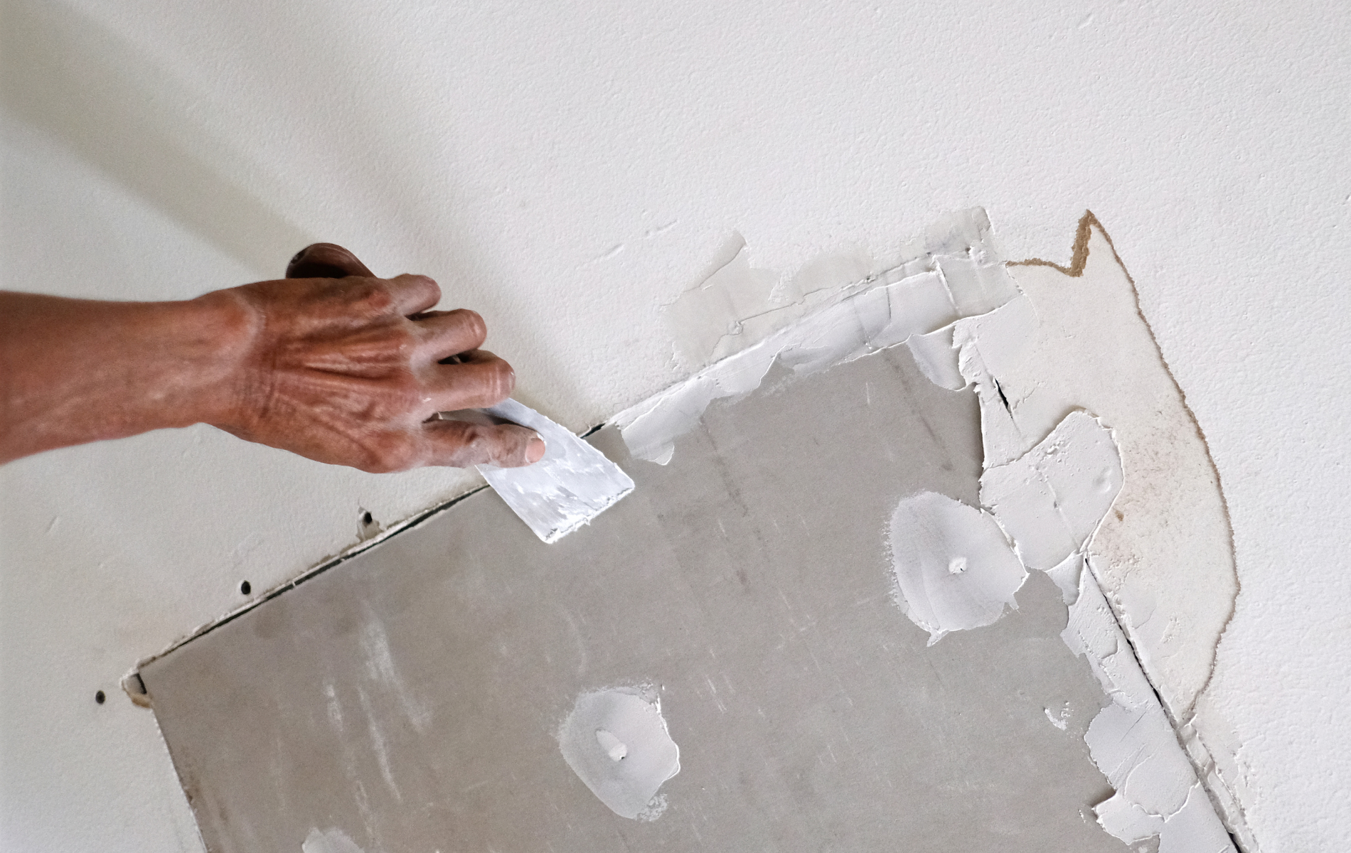 Person uses a putty knife to apply compound to repair a drywall section.