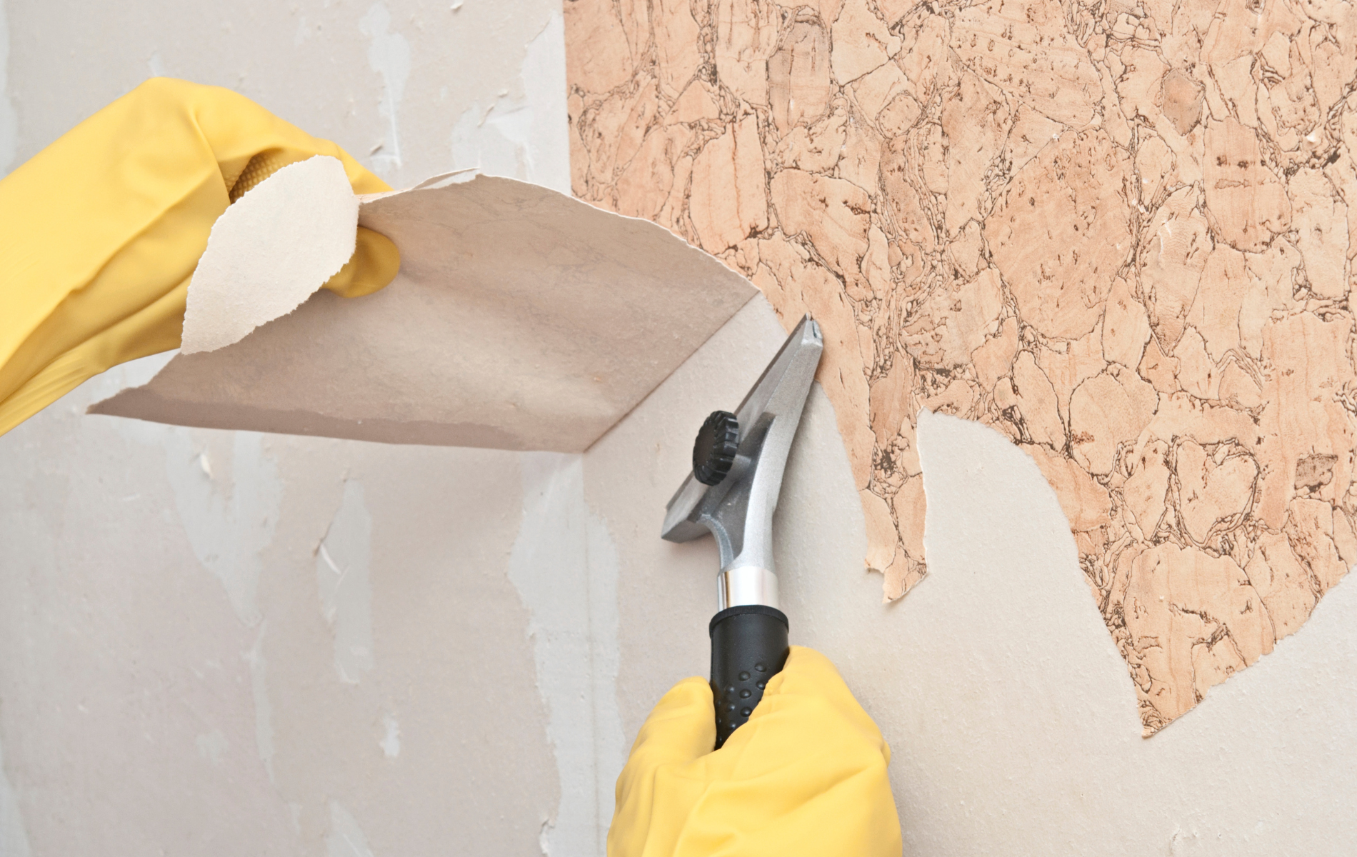 Person wearing yellow gloves removing cork wallpaper with a scraper tool.