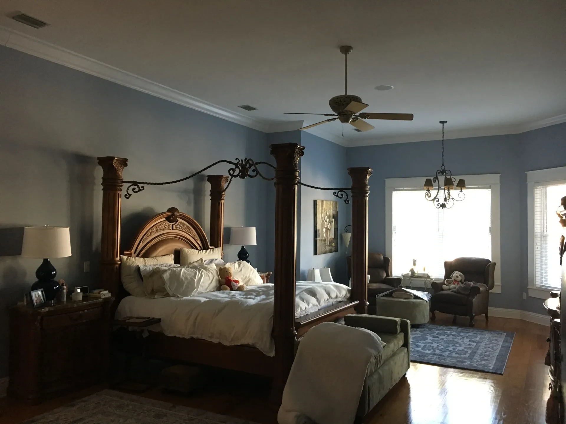 Bedroom with a four-poster bed, light blue walls, and a seating area near windows.