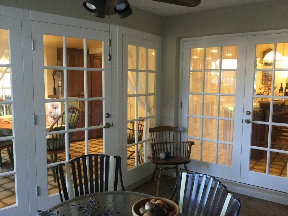 Sunroom with white French doors, table, chairs, and views of other rooms with warm lighting.