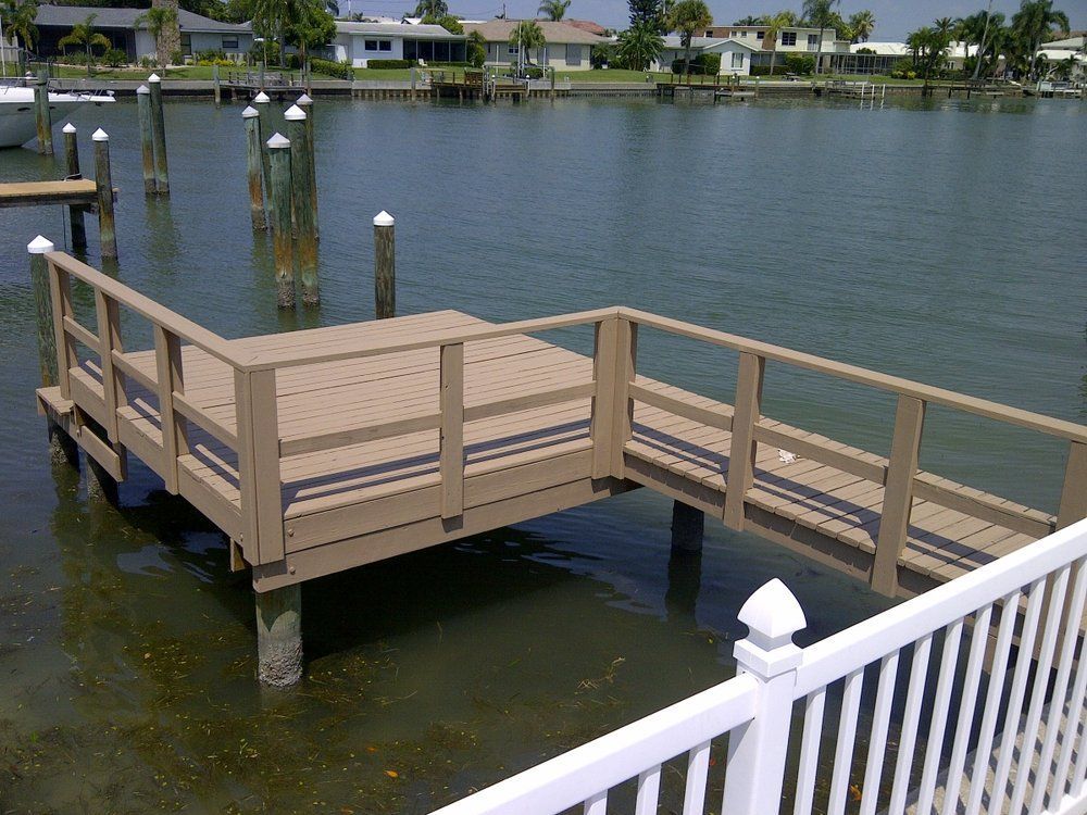 Wooden dock with railing extends into a body of water, residential area in background.