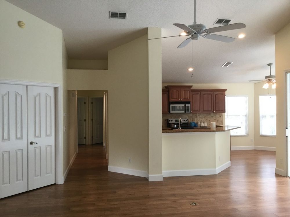 Interior view of a home with a kitchen, hallway, and wooden floors.  Includes closed closet doors and beige walls.