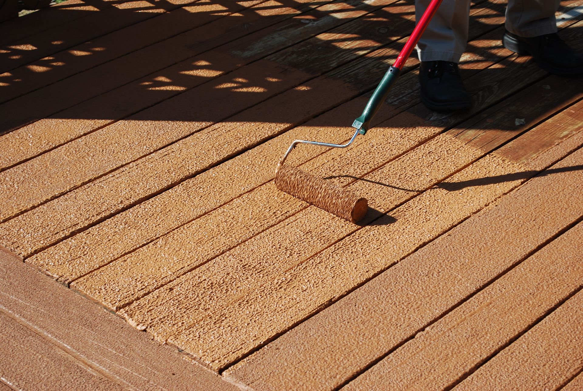 Person rolling brown deck stain onto wooden deck planks.