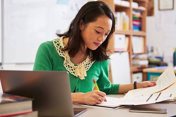 A woman is sitting at a desk with a laptop and a notebook.