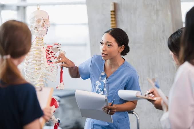 A nurse is holding a skeleton model in front of a group of students.
