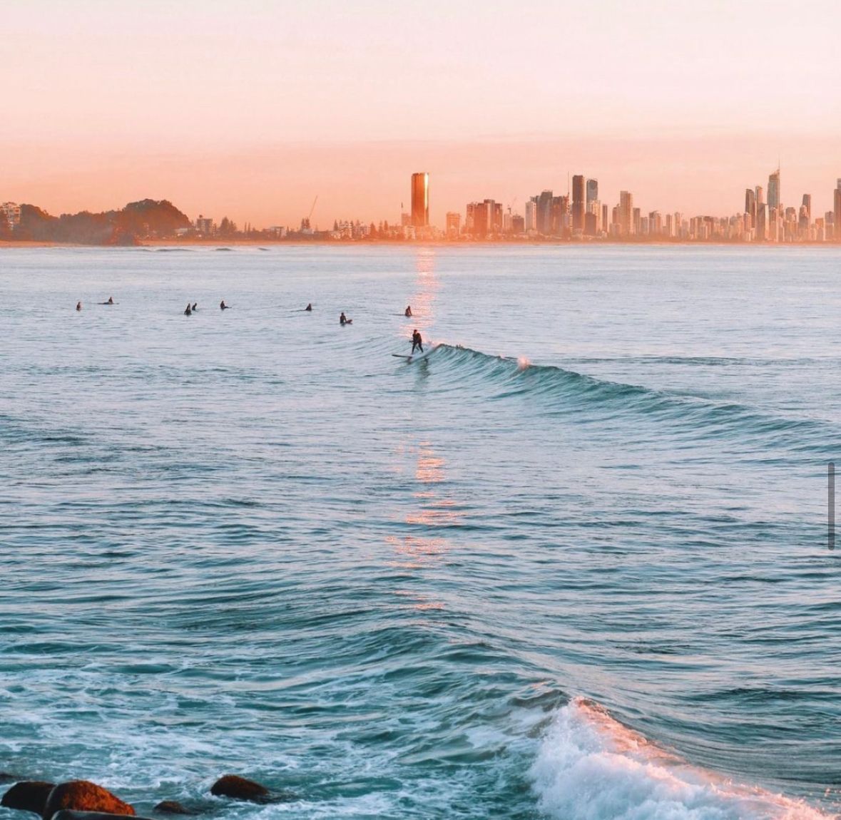 A Group Of People Are Surfing In The Ocean With A City In The Background — One Lane Financial In Burdell, QLD