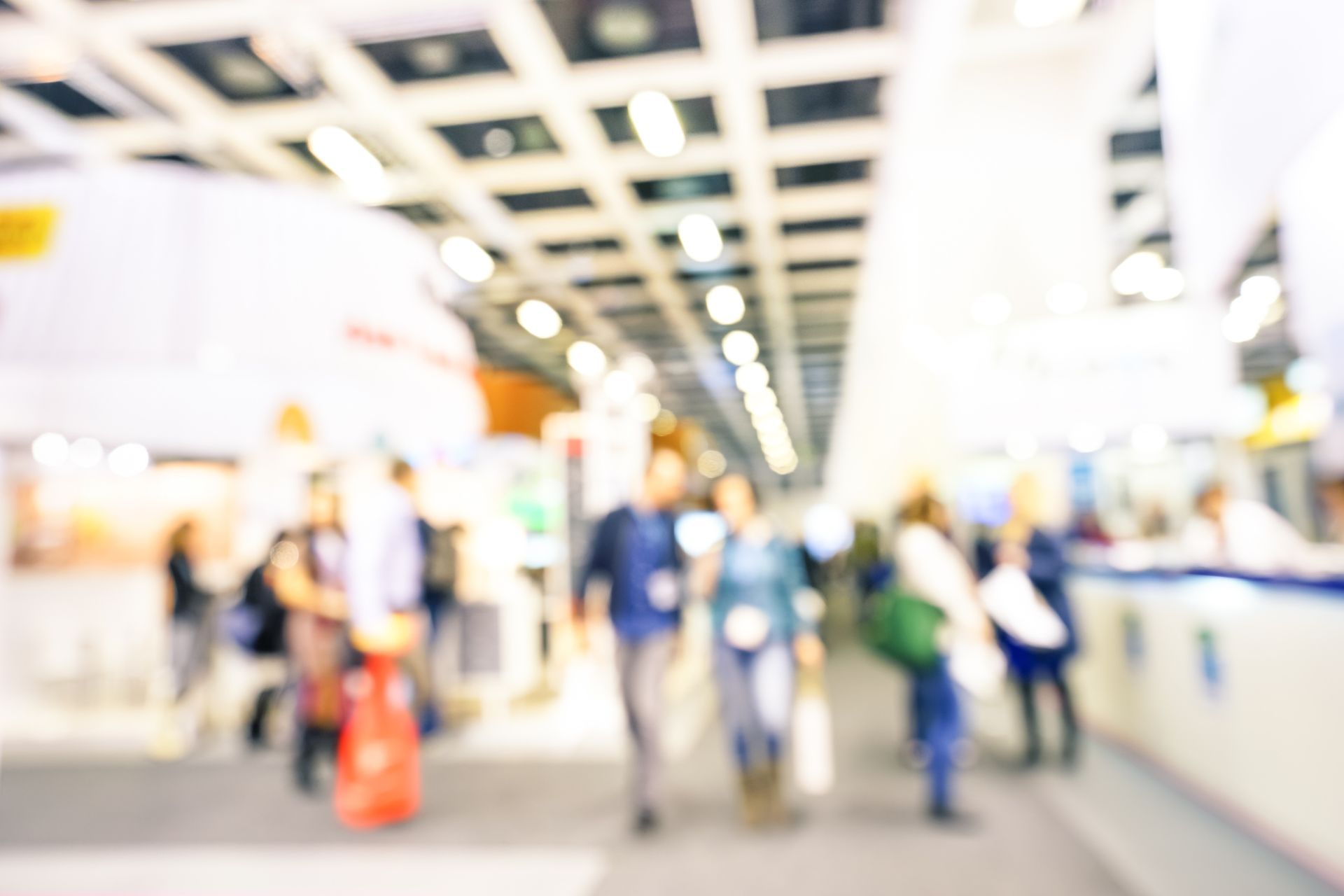Blurry picture of convention with people walking about, where display stands usually are placed.