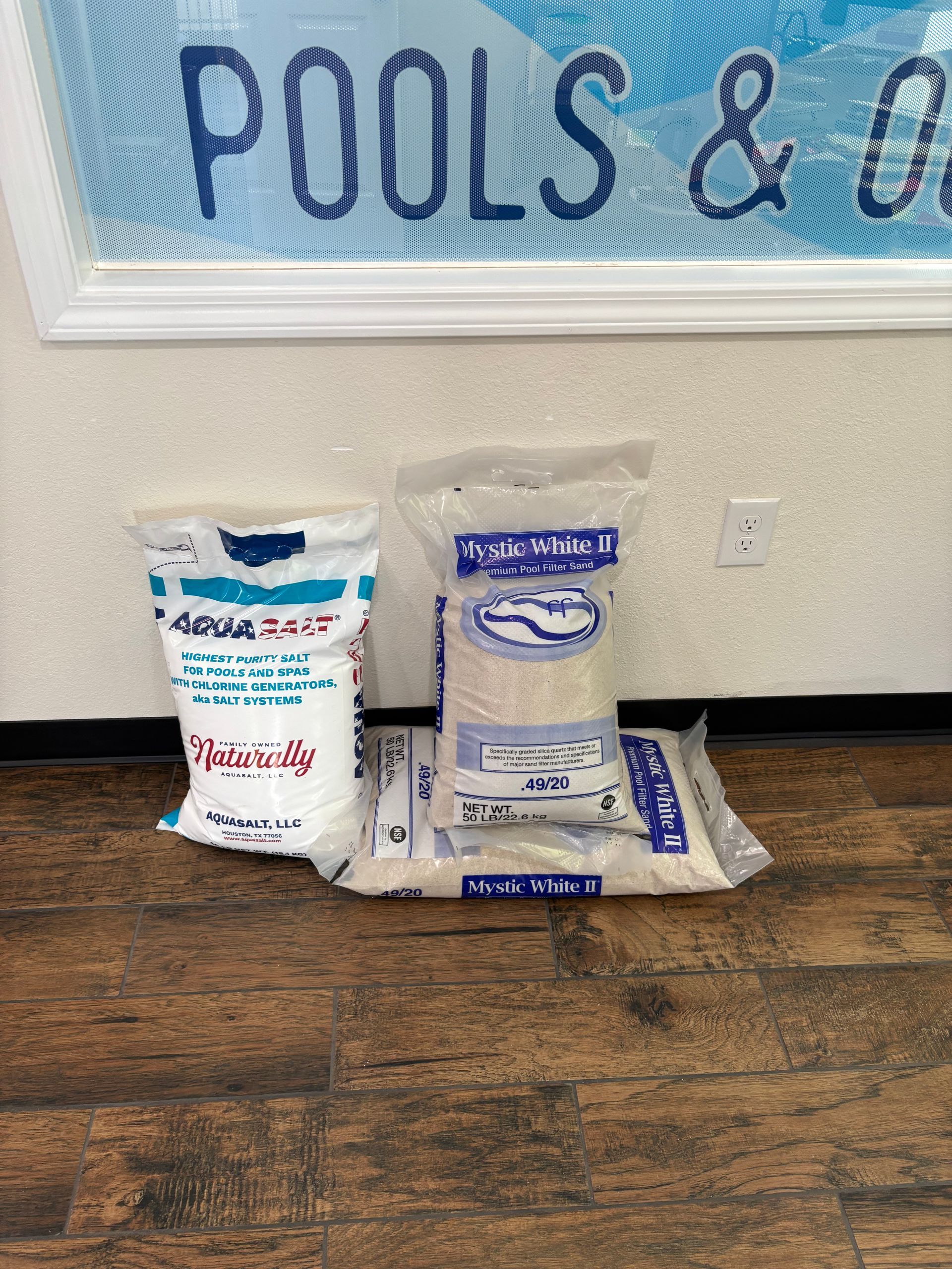 Three bags of pool chemicals are sitting on a wooden floor.