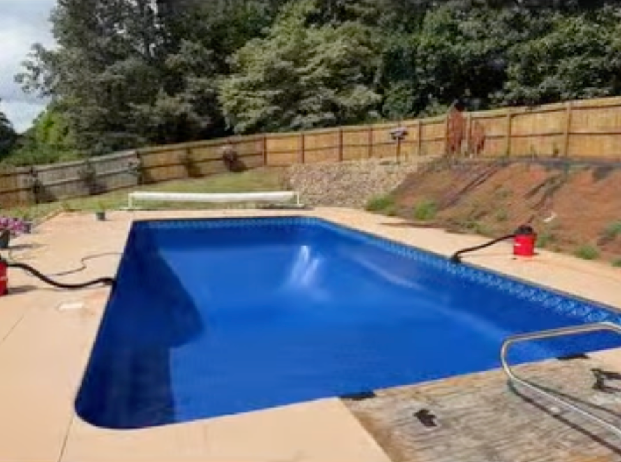 A large blue swimming pool with a wooden fence in the background.