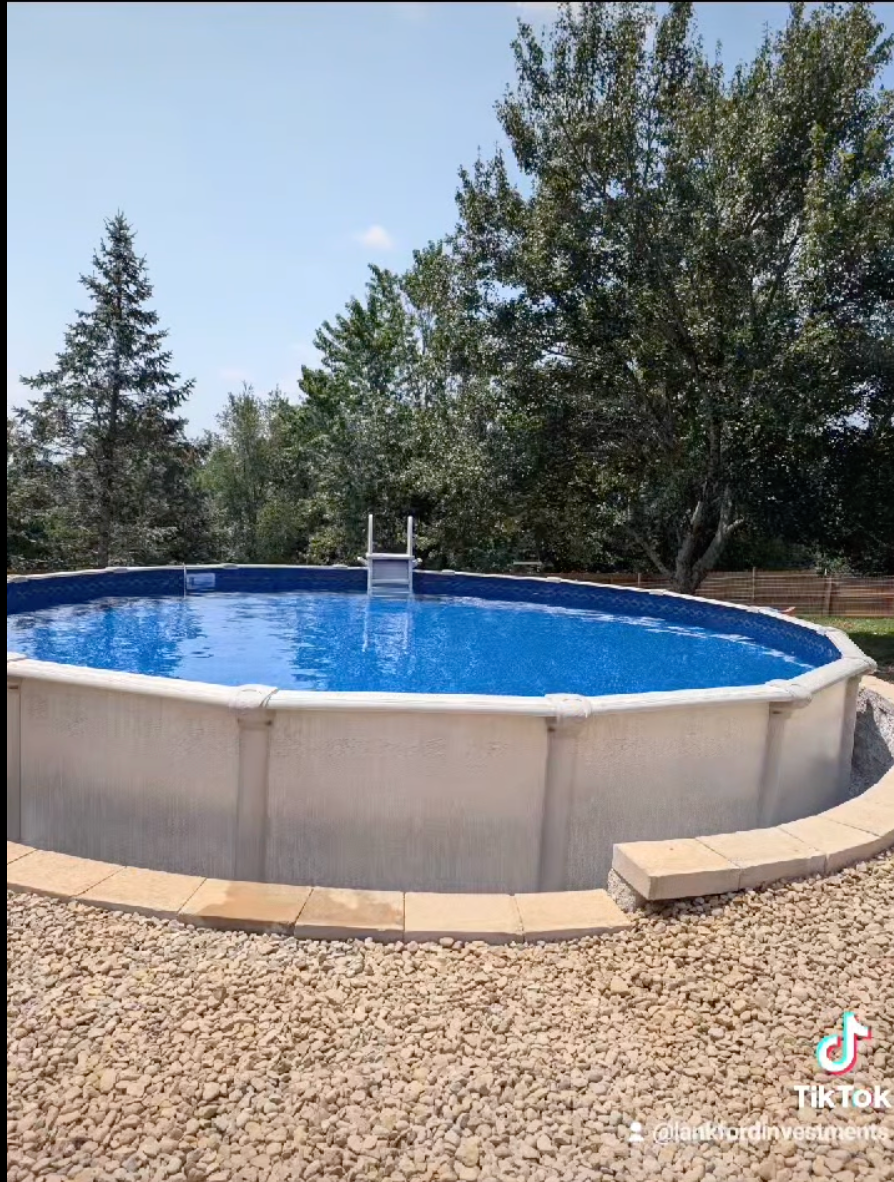 A large swimming pool with a ladder in it is surrounded by trees.