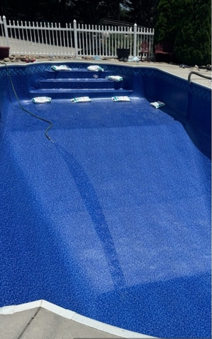 A blue swimming pool with stairs and a white fence in the background.