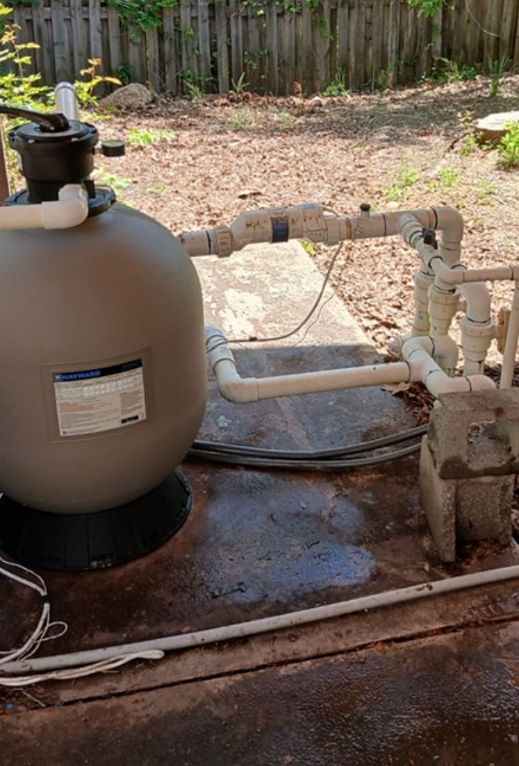 A swimming pool filter is sitting on the ground next to a fence.