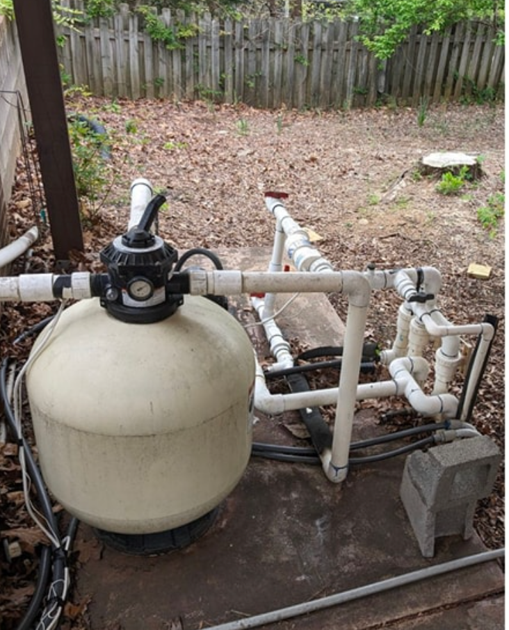 A pool filter is sitting on top of a pile of pipes.