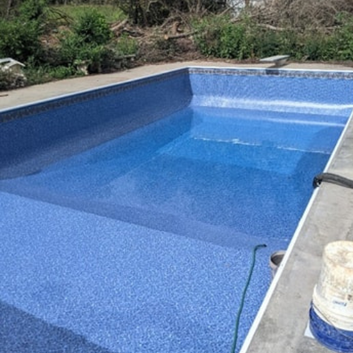 A large blue in-ground swimming pool is in a backyard.