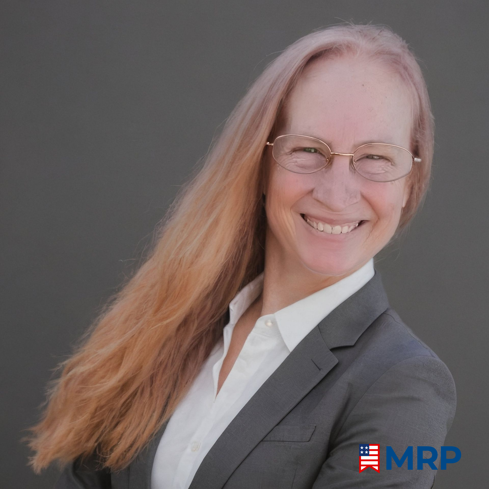 A woman is sitting at a desk with a laptop and a vase of flowers.