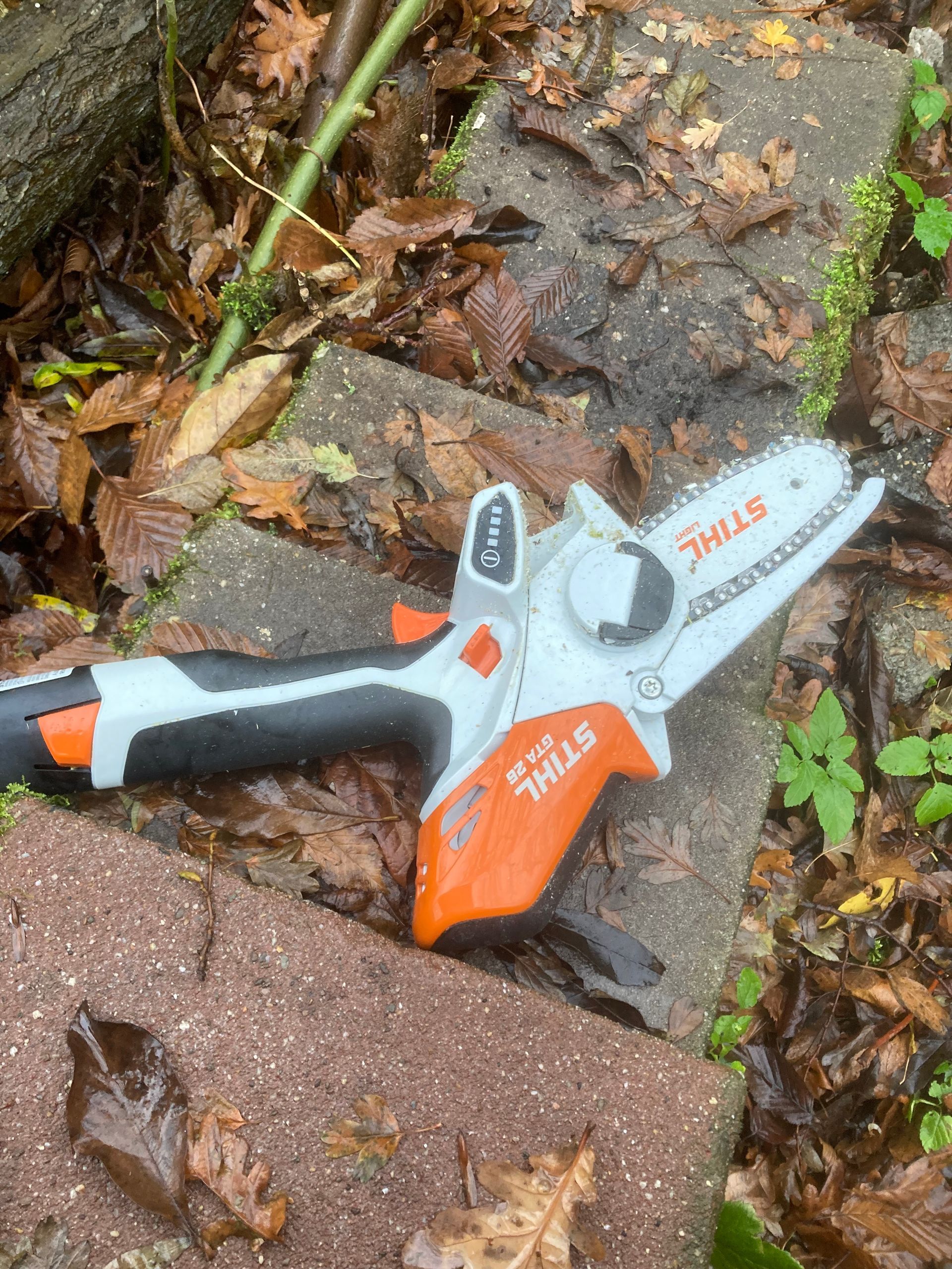 A Stihl GTA 26 cordless garden pruner laying on stone, surrounded by leaves.