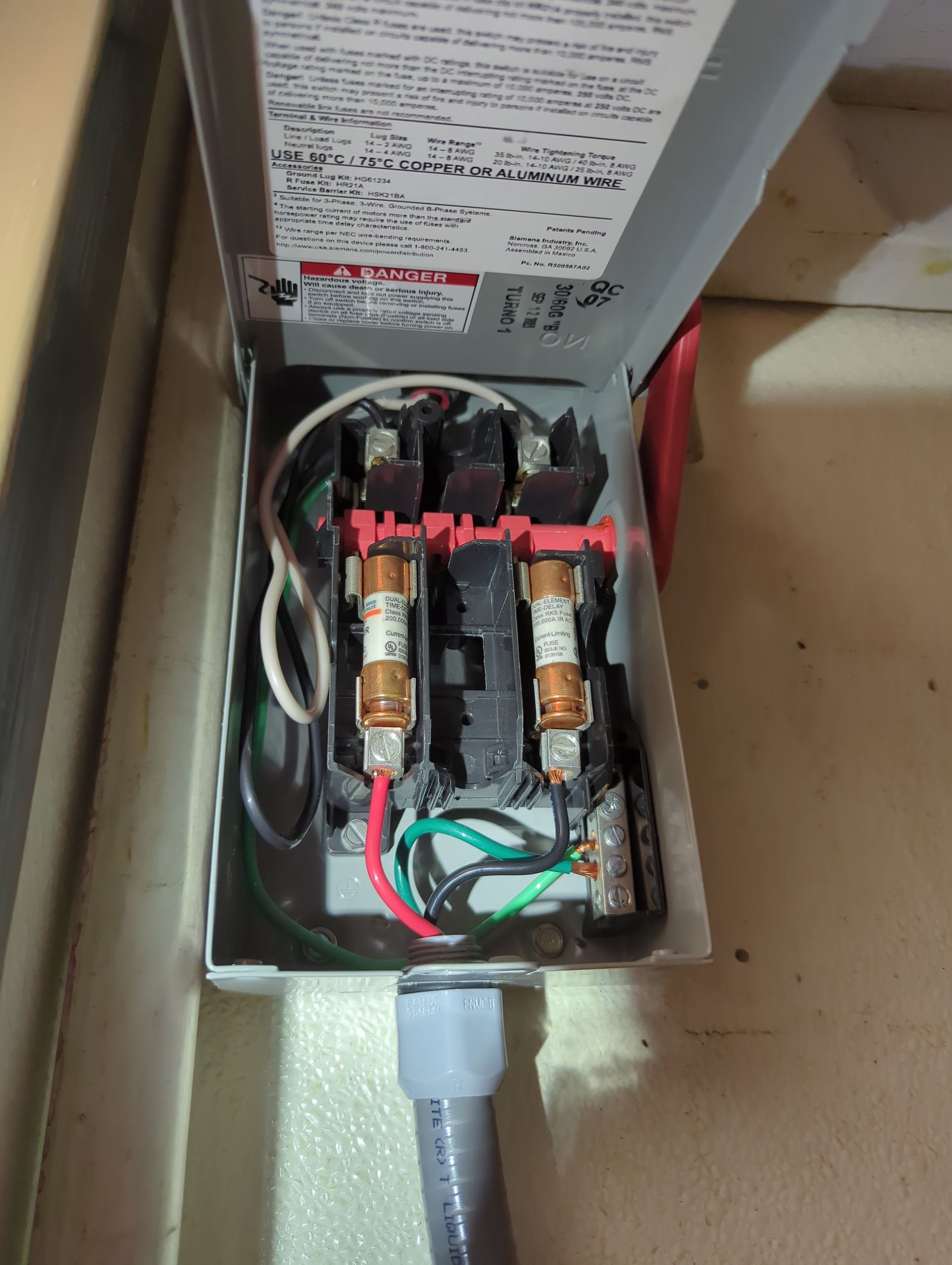 An open electrical disconnect box showing two cylindrical fuses and wiring connections inside a gray metal casing.