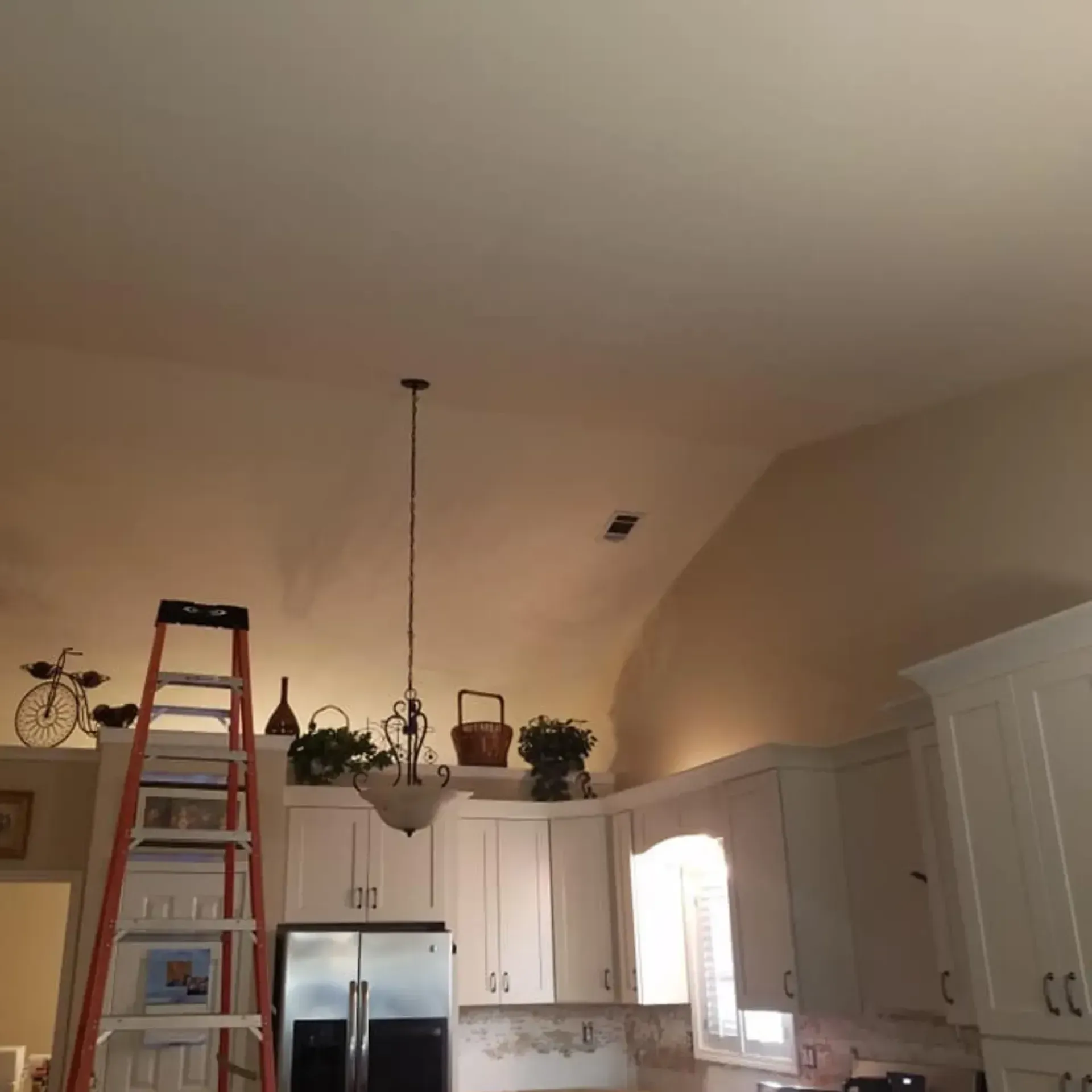 Ladder next to kitchen cabinets with a high ceiling, a light fixture, and decor