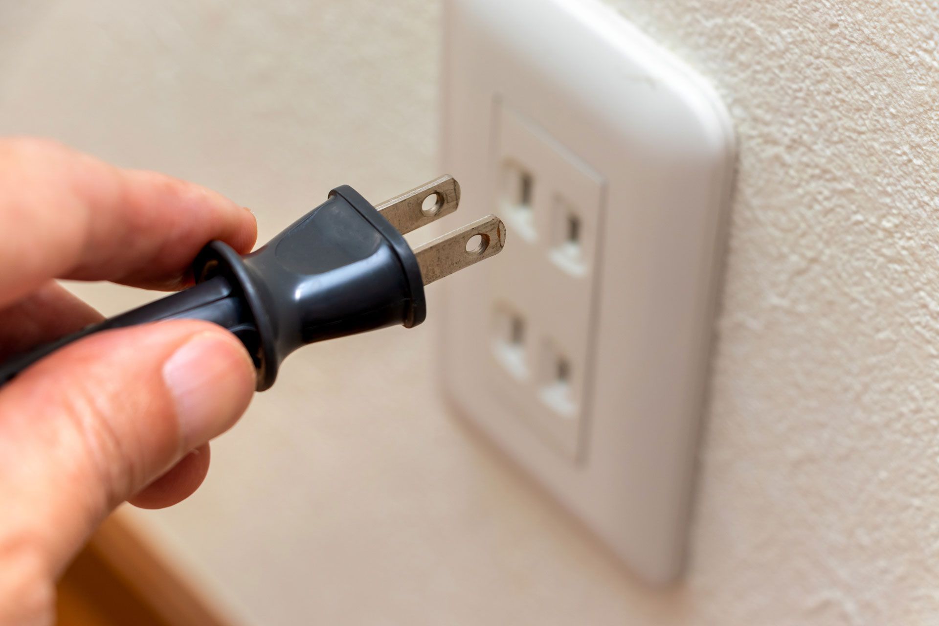 Electrician wearing blue gloves uses wire strippers on a green electrical wire near a wall-mounted light switch.