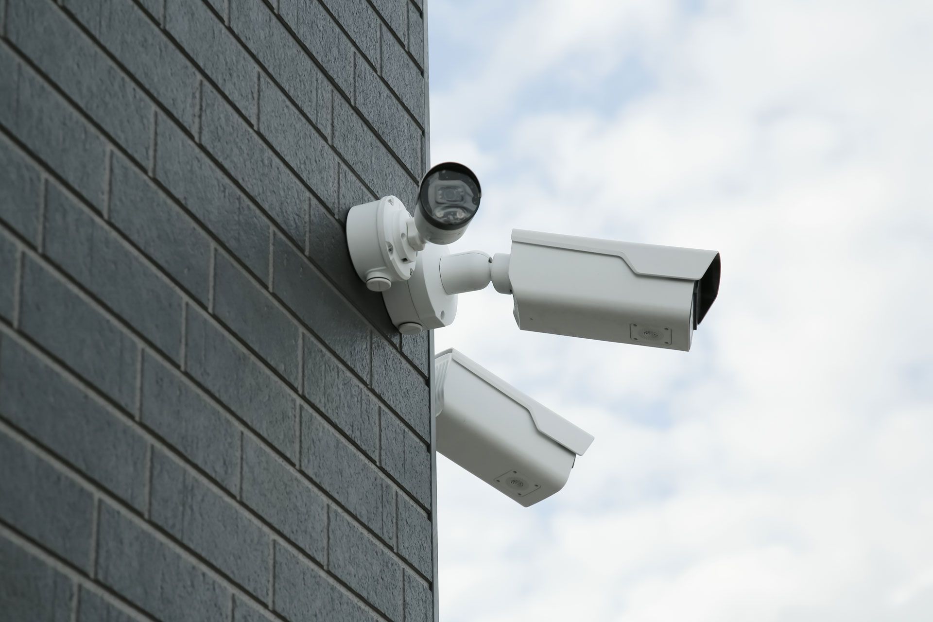 A person uses a screwdriver to install or adjust a white outdoor security camera mounted on a wall.