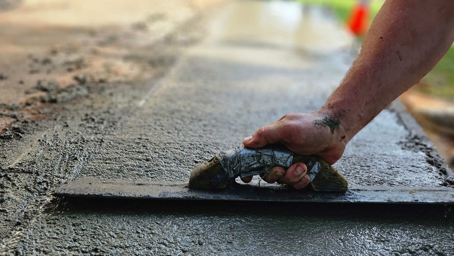 Hand smoothing wet concrete with a trowel outdoors.