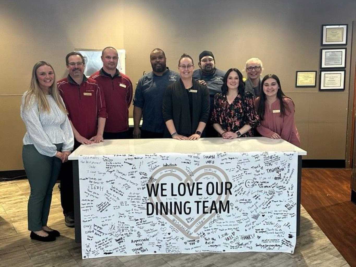 Group of dining staff smiling behind a table that says 