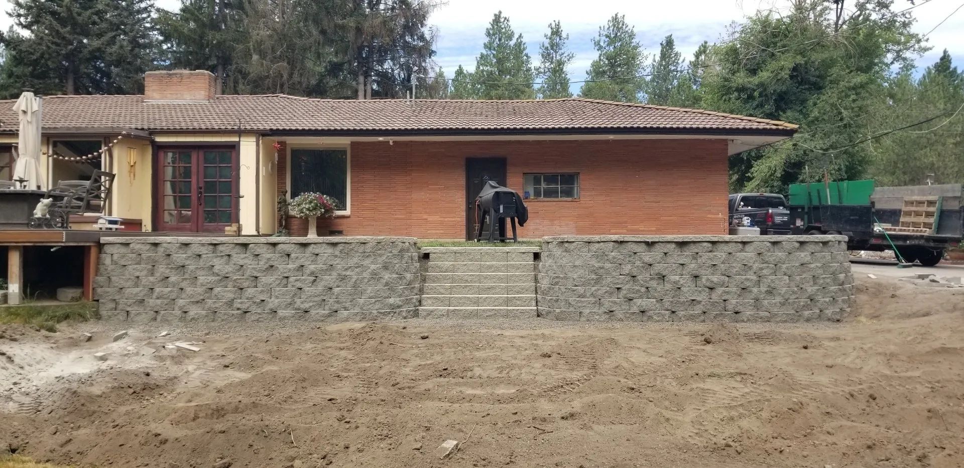 A house with a brick exterior and a low stone wall in front. A dirt yard stretch