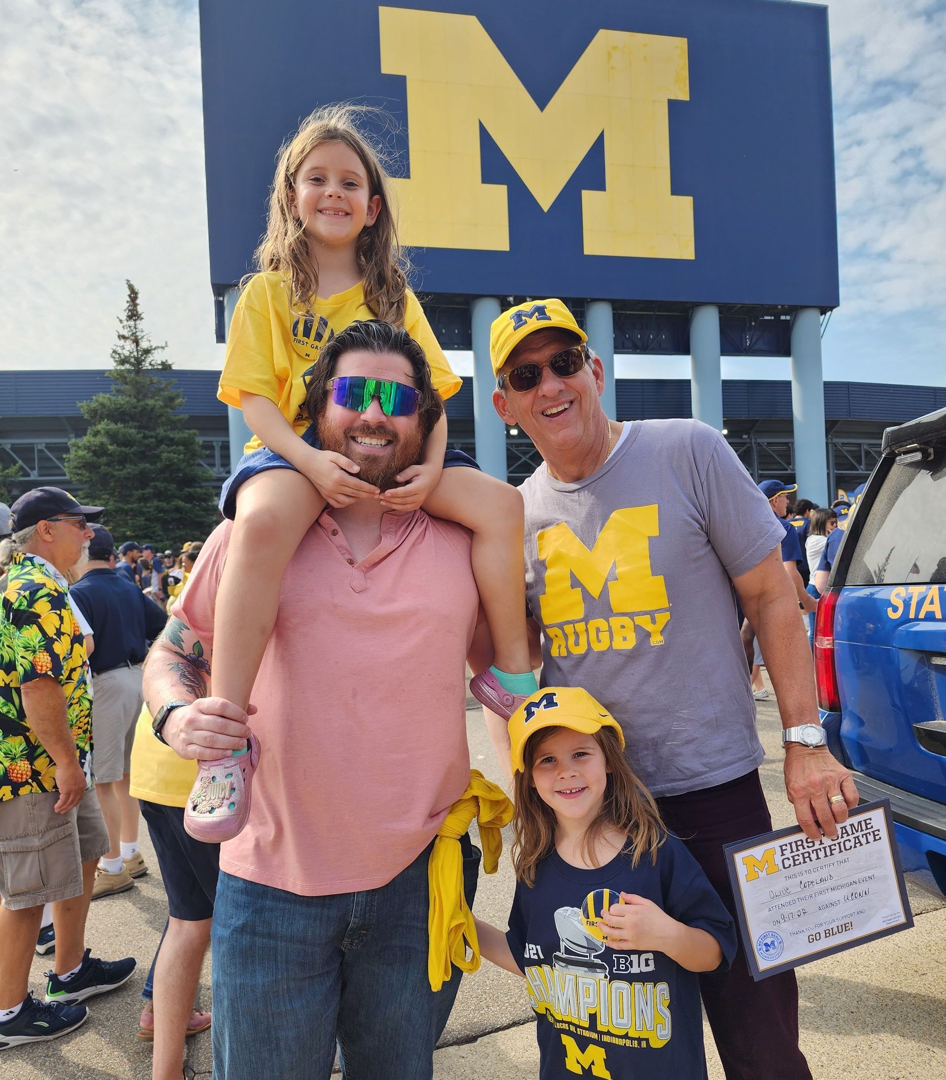 A man is carrying a little girl on his shoulders in front of a large m sign