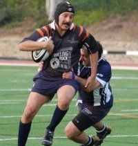Two men are playing rugby on a field and one of them is wearing a helmet.
