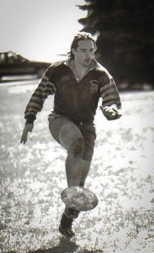 A black and white photo of a man kicking a rugby ball