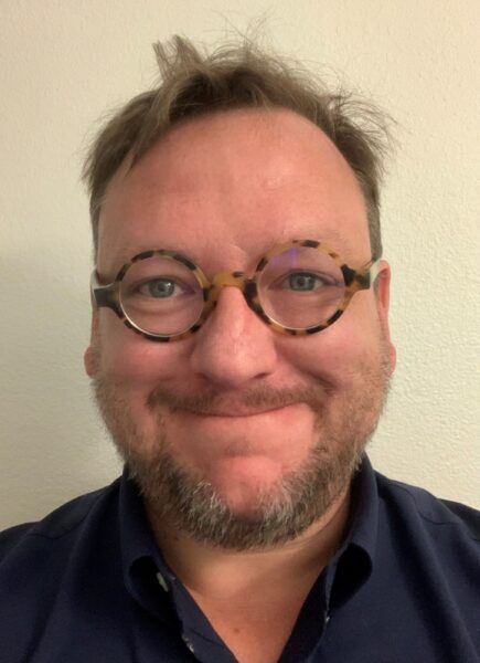 A man with glasses and a beard is smiling for the camera.