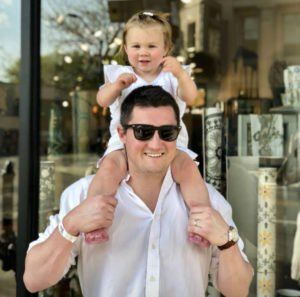 A man wearing sunglasses is carrying a little girl on his shoulders.