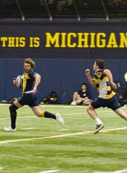 Two men running on a field in front of a sign that says this is michigan