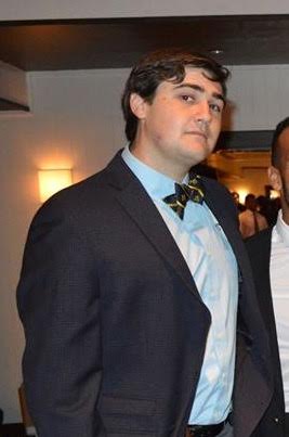 A man in a suit and bow tie is standing next to another man.