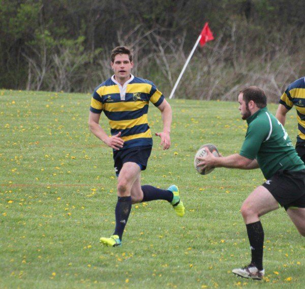 A man in a yellow and blue striped shirt is running with a rugby ball