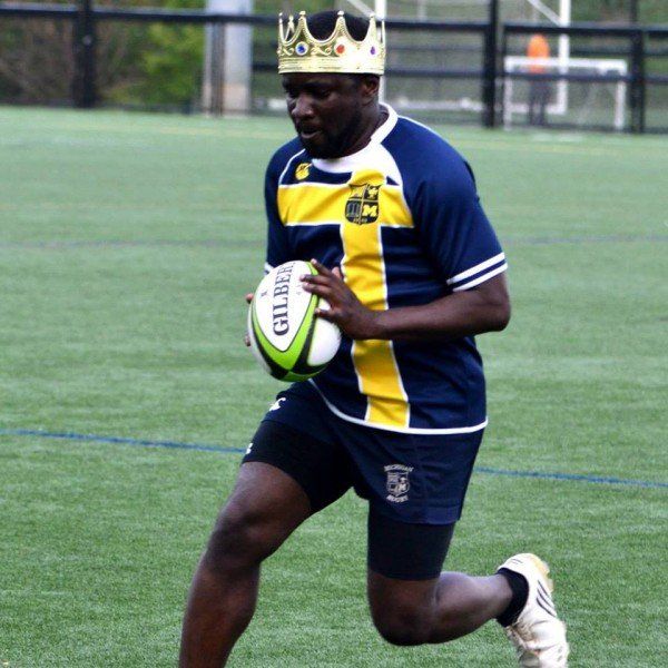 A man wearing a crown is running with a gilbert rugby ball