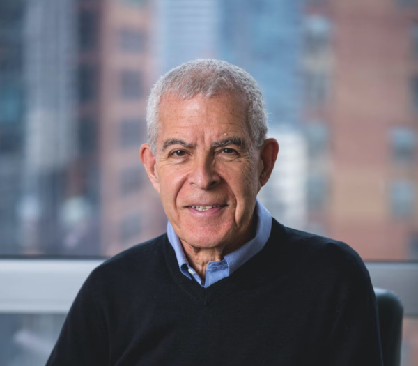 A man wearing a black sweater and a blue shirt is smiling for the camera.