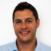 A man with a beard is smiling for the camera while wearing a blue shirt.